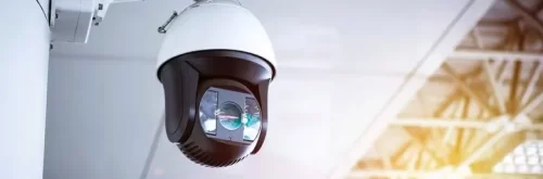 Caméra de surveillance blanche et fixée sur un mur avec un objectif motorisé